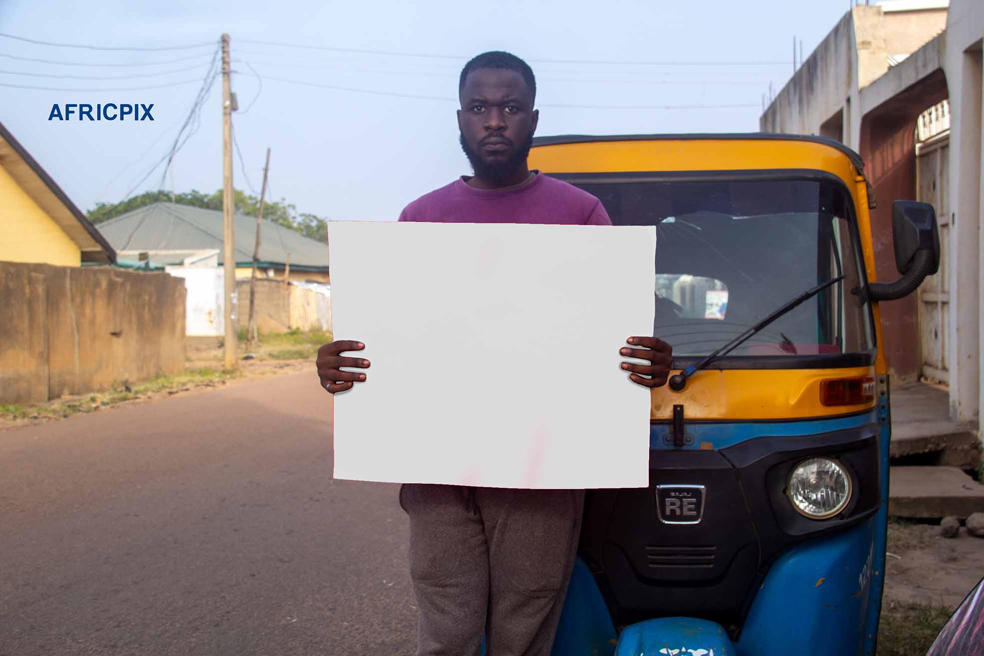 A Sad African tricycle rider, also known as Keke or Maruwa rider, standing with his tricycle behind him, holding a placard with an angry expression